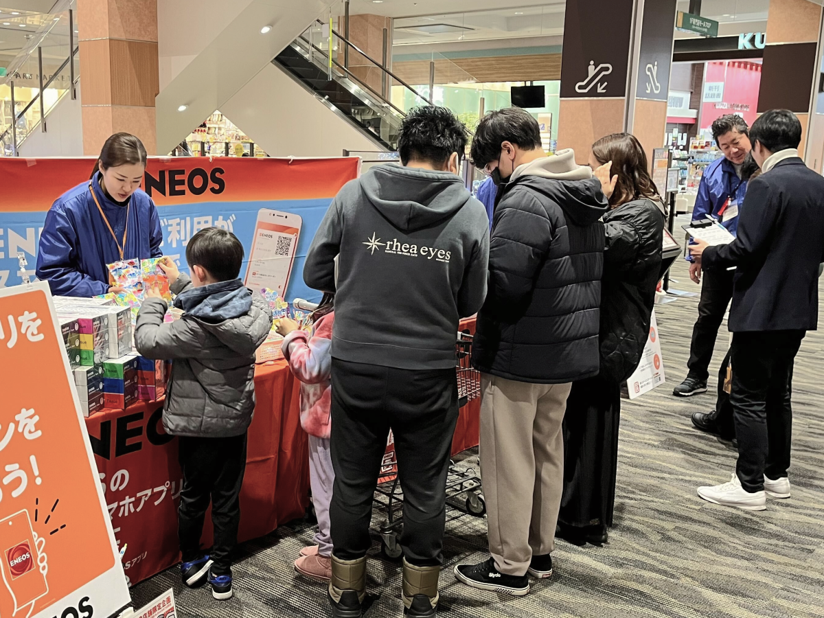 イベントでスタッフが子どもに景品を渡しており、その隣ではスタッフがお客様にアンケートを取っている様子