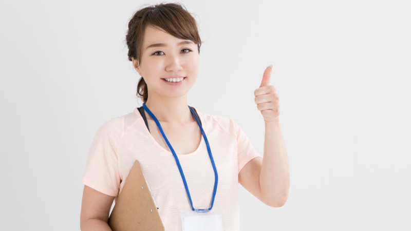 クリップボードを持った女性が左手の親指を立てている様子