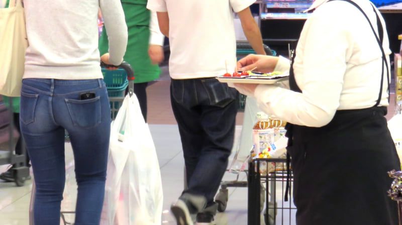 試食販売スタッフが、スーパーの試食コーナーで、商品を手に持っている様子