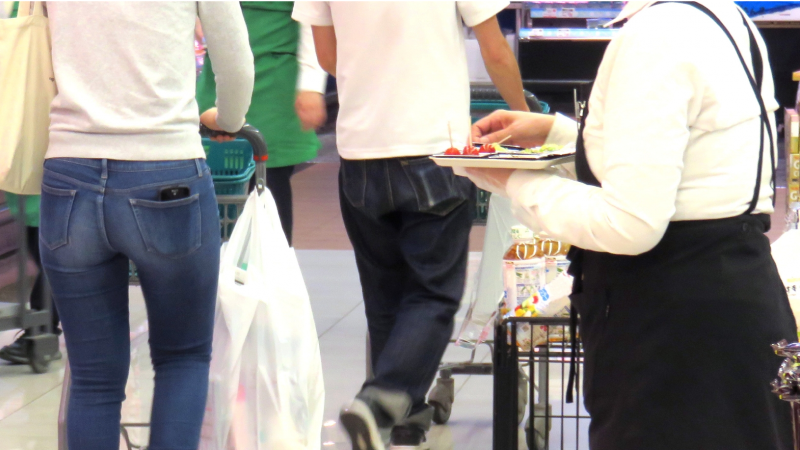 試食販売スタッフが、スーパーの試食コーナーで、商品を手に持っている様子